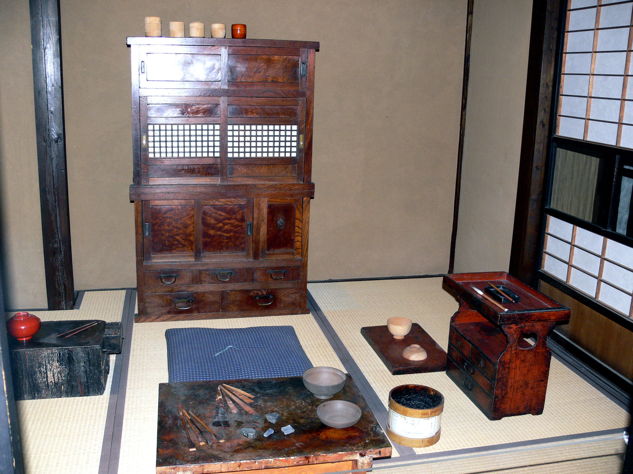 畳の上に作業台や刷毛、漆桶が並ぶ漆工房の再現展示